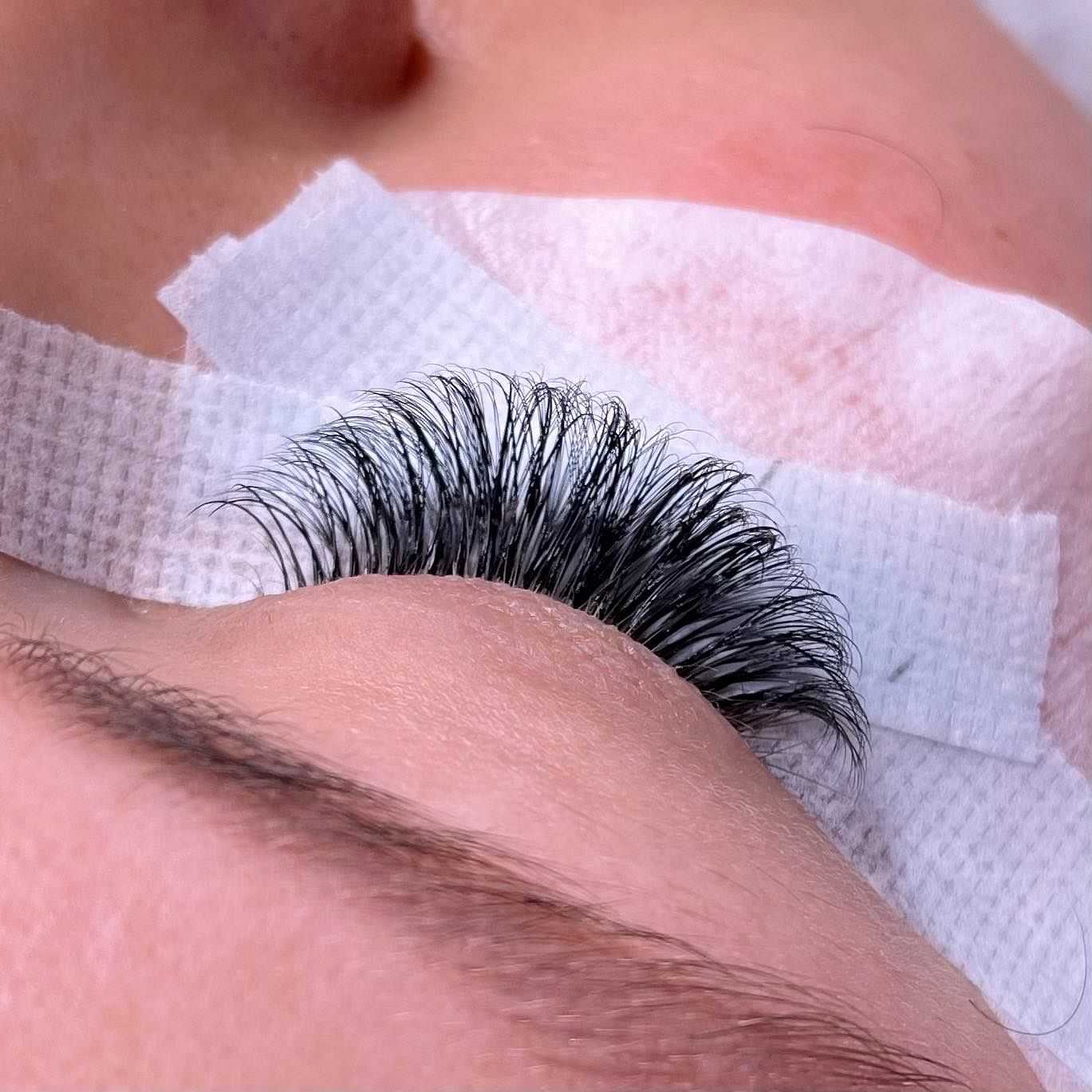 Close-up of a person receiving eyelash extensions with tape holding down lashes.