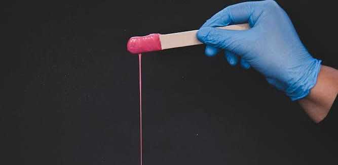Gloved hand holding a stick with pink slime dripping against a dark background.