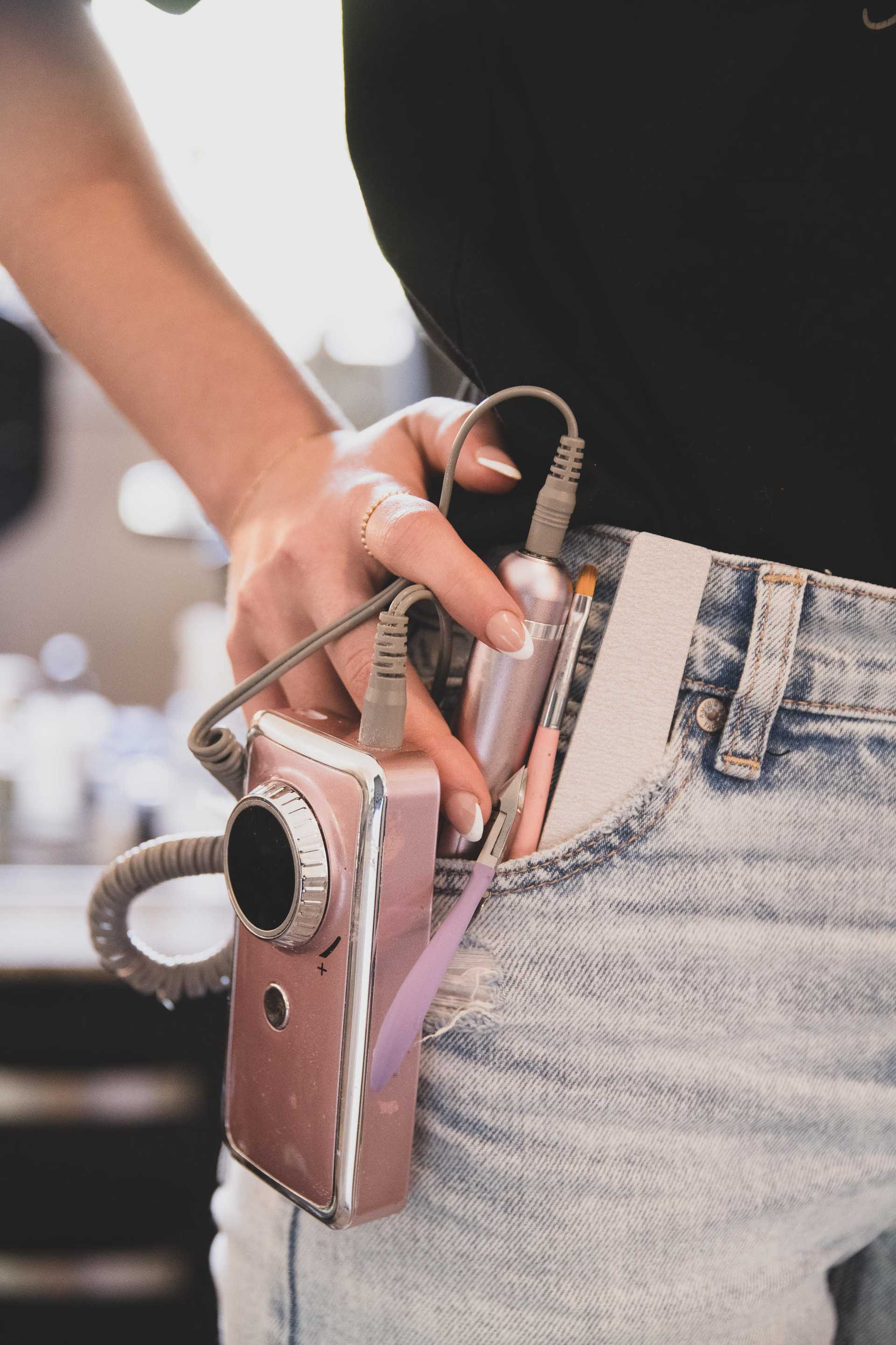 Person with a camera and small electronic device clipped to the front pocket of their jeans.