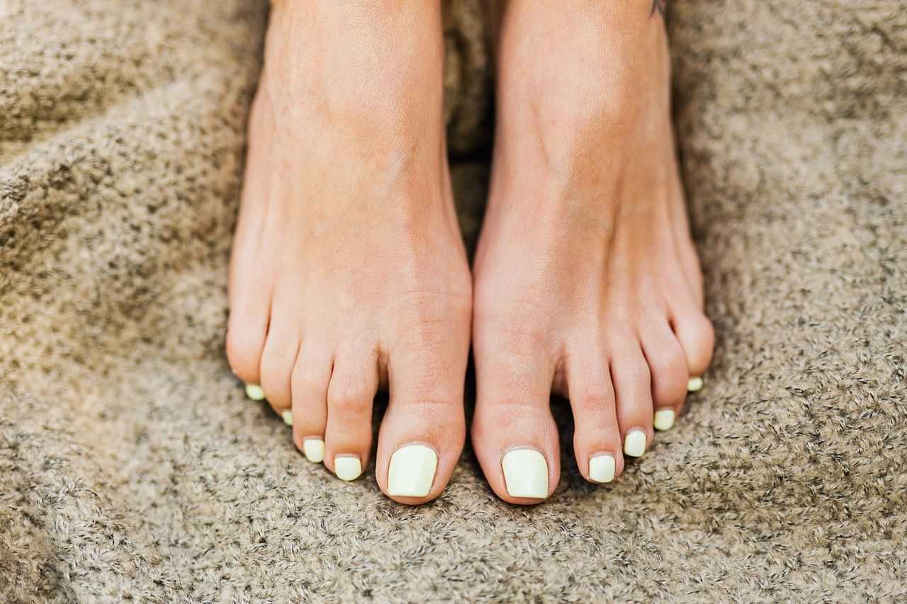 Close-up of bare feet with yellow nail polish on toes.