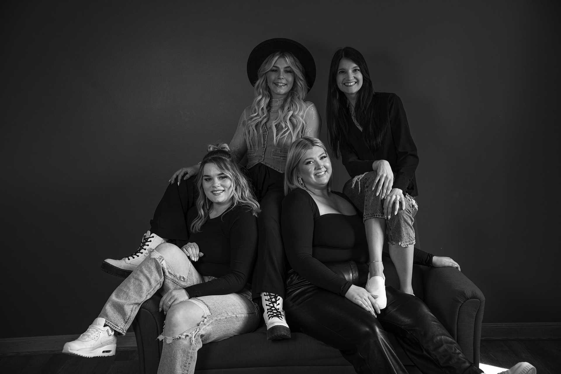 Black and white photo of four women sitting and smiling on a couch against a plain background.