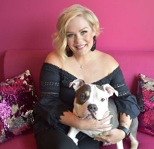 Woman smiling, holding a white and gray dog on a pink couch.